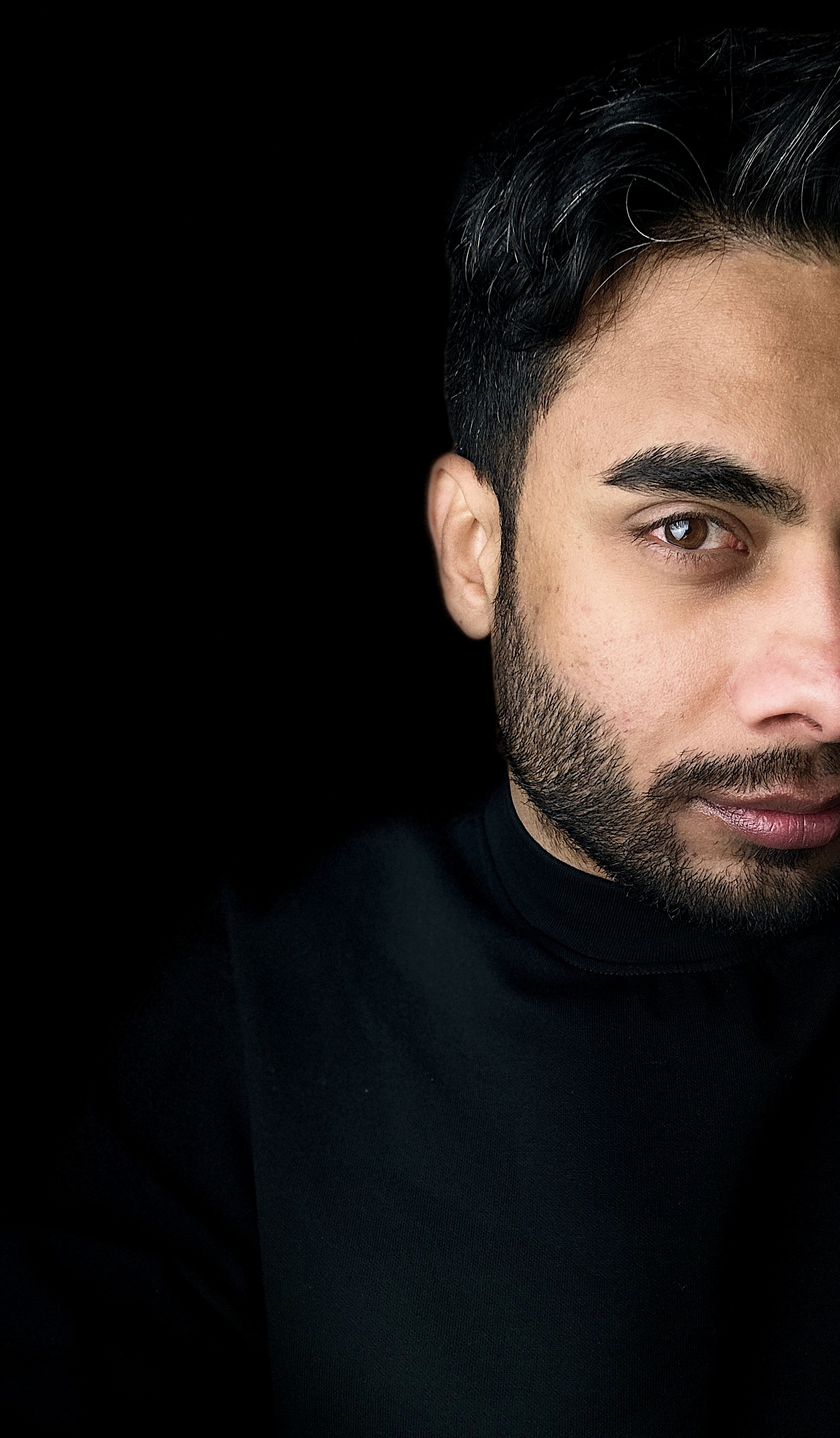 Portrait of Artan Davoodi wearing a black turtleneck against a black background